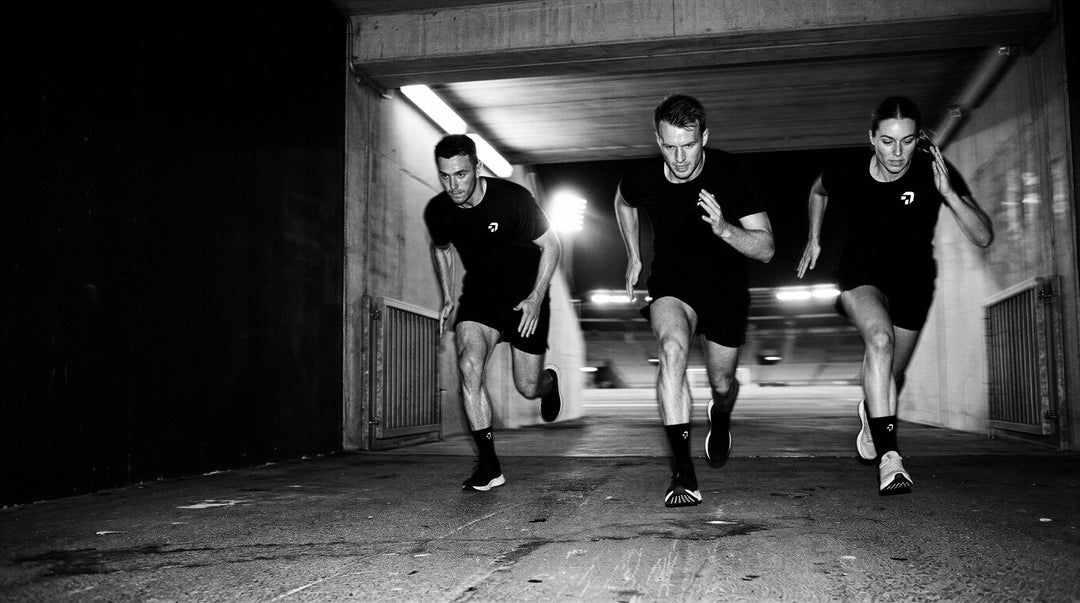 Zwart-wit: drie sporters in zwarte shirts sprinten een tunnel uit, op sokken van Create Performance